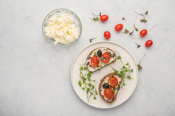 Homemade sandwiches with baked tomatoes, olives, cheese and herbs on bread on a white ceramic plate