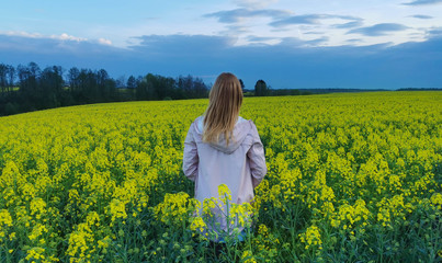Fototapeta premium Beautiful blonde girl in a rape field before the storm. Photos from the back.