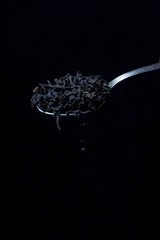 Obraz na płótnie Canvas loose leaf tea falls from a teaspoon on a black background