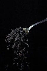loose leaf tea falls from a teaspoon on a black background