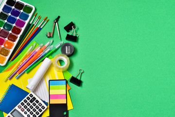 Education concept. Back to school. Top view of colorful school supplies with notebooks, pencils, calculator, clips, pens on a green background. Place for text