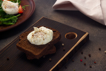 Healthy breakfast of toast with poached egg, tomatoes on a dark background