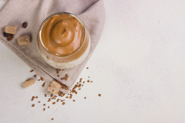 Dalgona Coffee in a transparent cup at white slate table top.