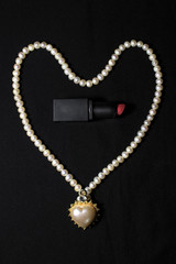 Red lipstick isolated on black background. Love heart design with white garland.