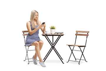 Young woman in a casual dress sitting at a cafe and using a mobile phone