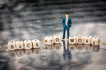 Miniature model of man and wooden cubes with back to work inscription strung on a thread on reflective table.