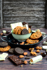 Chocolate and oatmeal cookies, white and dark chocolate, almonds and chocolate bars on a dark wooden background. Sweets and dessert