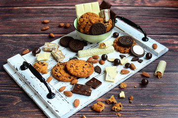 Composition with white and milk types of chocolate, chocolate and oatmeal cookies and nuts on a wooden white tray