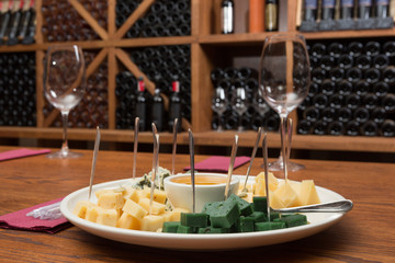 plate with appetizers for wine, several varieties of cheese and honey, on the background of shelving with wine