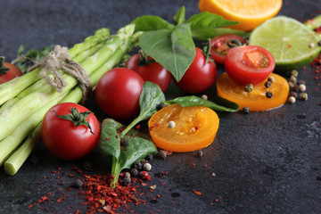 Fresh raw vegetables and herbs, asparagus, red cherry tomatoes, yellow tomatoes, lemon, lime, spinach, basil and spices on a black background. Background image, copy space