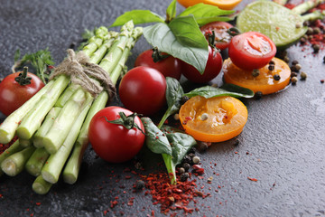 Fresh raw vegetables and herbs, asparagus, red cherry tomatoes, yellow tomatoes, lemon, lime, spinach, basil and spices on a black background. Background image, copy space