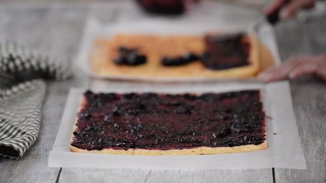 Girl spreading jam on a flat sheet of cake to make a cake with vertical layers at home.