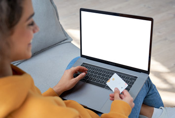 Happy hispanic female shopper customer holding credit card paying online on laptop mock up white...