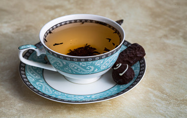 Cup of black tea with sweets on a beige textural background.