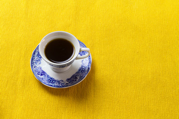 Chinese porcelain coffee cup on top of yellow placemat.