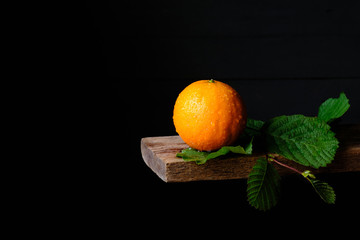 Still life of fresh orange with green leaves on black background