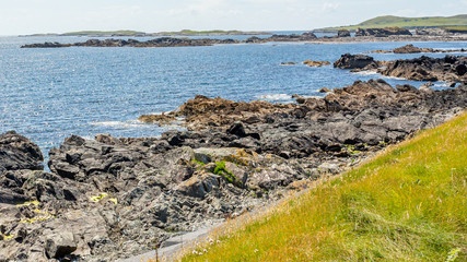 Rocky coastal shoreline at Inishbofin or White Cow Island with the horizon over the Atlantic Ocean, sunny spring day with a blue sky and white clouds in County Galway, Ireland