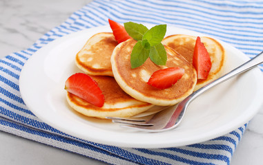 Pancake in a plate with strawberries decorated with mint on a marble background