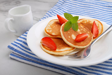 Pancake in a plate with strawberries decorated with mint on a marble background