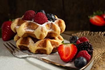 Dessert of Belgian waffles with strawberries, summer berries on plate with canvas on dark old wooden dramatic background. Horizontal view. Menu, banner, poster, mock up. Rustic vintage style of