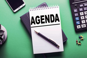 Notebook, pen and a cup of coffee on table. Notebook written Agenda, business concept.