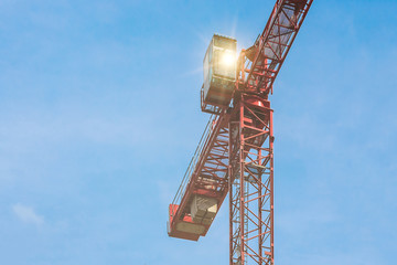 Naklejka premium Red tower crane with glare against blue sky with white clouds. Close up. Copy space.