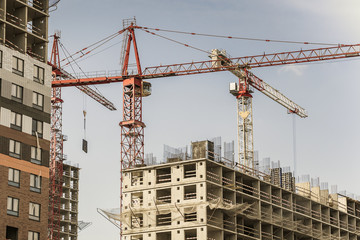 Several red cranes have been put to work on the construction of a modern multi-storey residential complex. Concept work for people with the profession of builder. Large construction site.