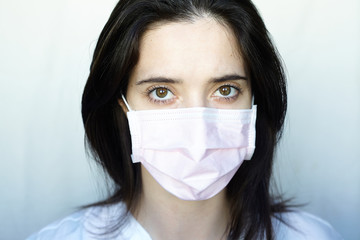 A woman in gloves and a protective mask stands on a light background in a white jacket. The concept of suppression of coronavirus