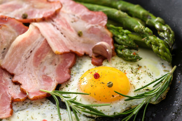 Fried asparagus with bacon, eggs and spices on a pan in close-up