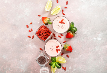 Fototapeta na wymiar Healthy blended drink. Organic vegan non dairy smoothie with strawberry and goji berries, chia seeds and lime. Gray background with copy space. Top view