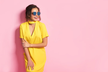 Beautiful girl wearing yellow dress and sunglasses posing on pink background in studio. Looking at...