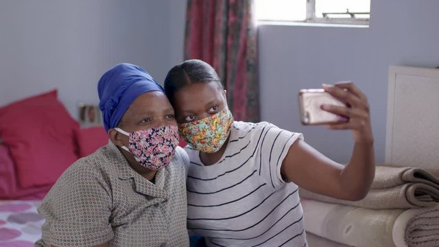 Black South African mother and daughter take selfies in their home wearing their covid-19 coronavirus protective masks. 