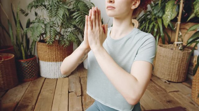 Arc midsection shot of young woman holding hands in prayer pose in front of her chest while practicing yoga at home