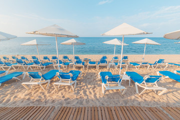 Fototapeta na wymiar Low season empty beach with sun loungers and straw umbrellas. in Crete town Hersonissos Day foto. Greece vacation.