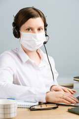 Woman in mask with headset, using computer and notebook.