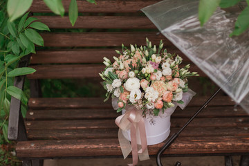 A large flower arrangement in a big white hat box in rainy day was created by a florist for a wedding gift. white freesia,  ranunculus asiaticus, eustoma flowers, roses and eucalyptus in flowers box