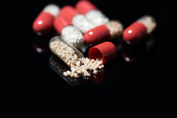 Red pills with white granules scattered on a black, glossy background. Medicinal capsules, pills.