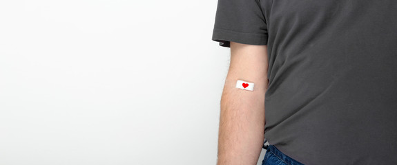 Blood donorship. Man in gray T-shirt hand taped with patch with red heart after giving blood on...