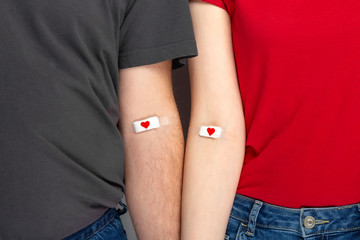 Blood donorship. Man in grey and woman in red T-shirt with hands taped patch after giving blood...