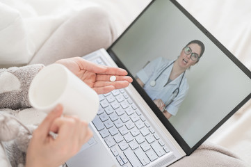 Unrecognizable woman drinks pills as prescribed by a doctor at an online consultation. Female doctor talking to a sick patient on a webcam. Girl with the flu on sick leave.