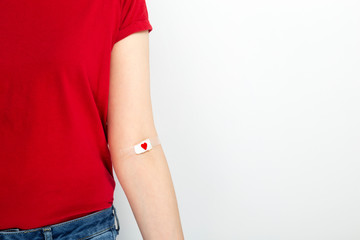 Blood donorship. Young girl in red T-shirt hand taped with patch with red heart after giving blood...