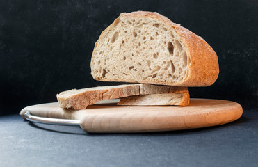 Beautiful bread made from rye and wheat flour on a wooden board on a black background. Sliced slices and half bread.