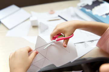 Child's hands cut paper with scissors. Child making geometric shapes. Home education.