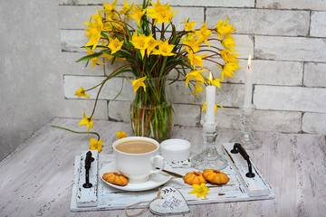 Spring decor. View of a white cup of coffee with foam and cookies on an old wooden tray and yellow tulips in a glass vase. Home relax