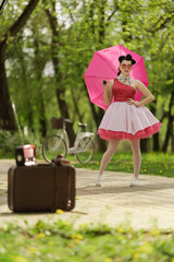 Retro style photo. A girl in a pink dress and hairstyle in the style of the 40-50s holds a pink...