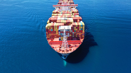 Fototapeta premium Aerial drone photo of huge container cargo Ship carrying load in truck-size colourful containers cruising deep blue open ocean Mediterranean sea 