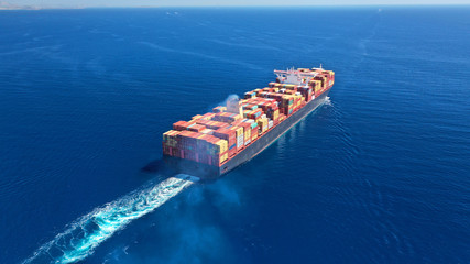 Aerial drone photo of huge container cargo Ship carrying load in truck-size colourful containers cruising deep blue open ocean Mediterranean sea 