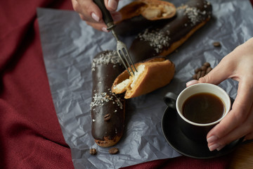 Fototapeta na wymiar Woman eating eclairs filled with cream, traditional french eclairs with chocolate and cup of espresso, selective focus.