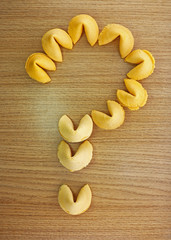 Fortune cookies in shape of a question mark on a wood background.
