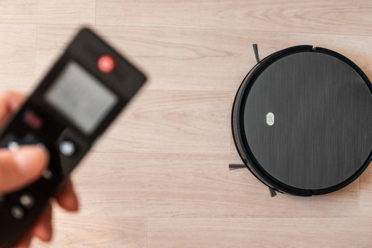 Black robot vacuum cleaner removes dusty floor cleaning in the bedroom using the remote control. Smart home, wireless technology concept